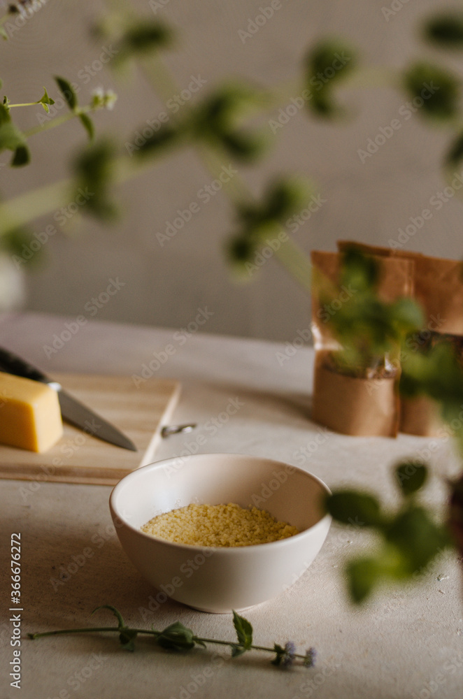 Pretty small ivory bowl with couscous porridge on table in the kitchen with cheese, spices and mint leaves decoration. Tasty and healthy vegetarian food isolated close up in rustic style Pretty small ivory bowl with couscous porridge on table in the kitchen with cheese, spices and mint leaves decoration. Tasty and healthy vegetarian food isolated close up in rustic style