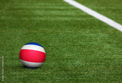 Costa Rica flag on ball at soccer field background. National football theme on green grass. Sports competition concept.