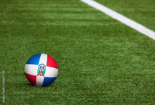 Dominican Republic flag on ball at soccer field background. National football theme on green grass. Sports competition concept.