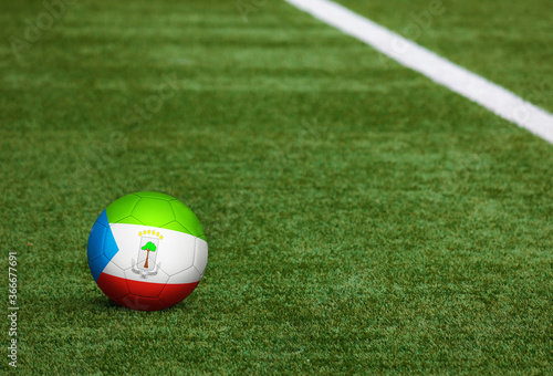 Equatorial Guinea flag on ball at soccer field background. National football theme on green grass. Sports competition concept.