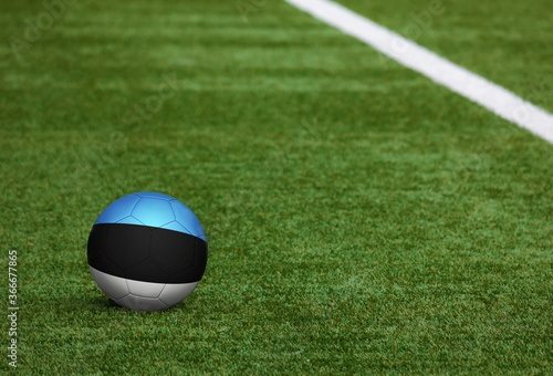 Estonia flag on ball at soccer field background. National football theme on green grass. Sports competition concept.