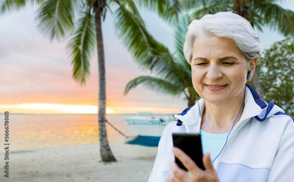 fitness, sport and healthy lifestyle concept - senior woman with earphones listening to music on smartphone over tropical beach background in french polynesia