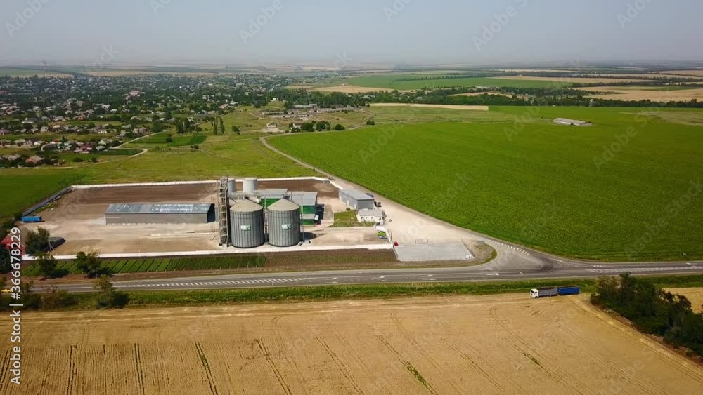 Aerial of grain elevator in front of wheat field. Quadcopter drone camera flying around flour or oil mill plant. Silos near farmland. Agriculture theme, a harvesting season. Tracking shot. Aerial of grain elevator in front of wheat field. Quadcopter drone camera flying around flour or oil mill plant. Silos near farmland. Agriculture theme, a harvesting season. Tracking shot.