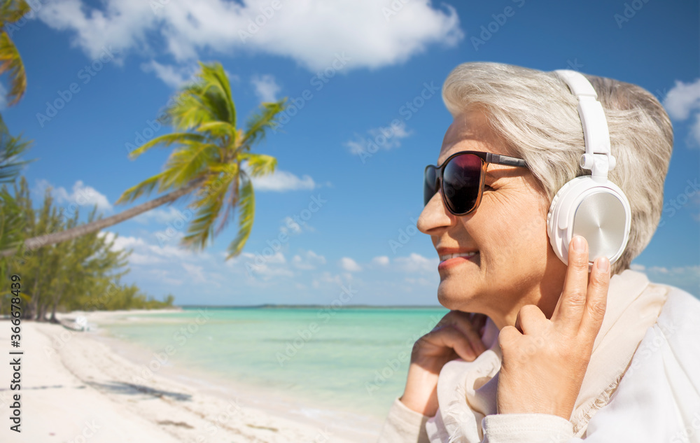 technology, old people and leisure concept - senior woman in headphones and sunglasses listening to music over tropical beach background in french polynesia