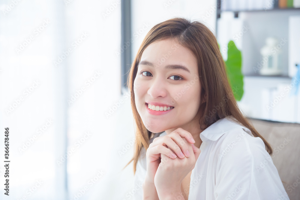 Beautiful asian woman sitting in living room ,looking at camera and toothy smile.