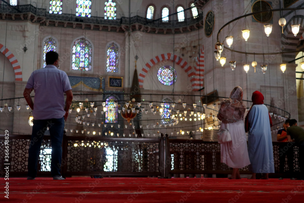 Two women wearing headscarves observe the interior of the Süleymaniye Mosque in Istanbul. A man who has not been wearing a scarf looks at them. Two women wearing headscarves observe the interior of the Süleymaniye Mosque in Istanbul. A man who has not been wearing a scarf looks at them.