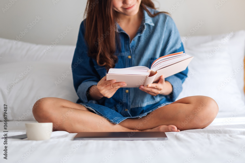 A beautiful young woman reading book while sitting on a white cozy bed at home A beautiful young woman reading book while sitting on a white cozy bed at home