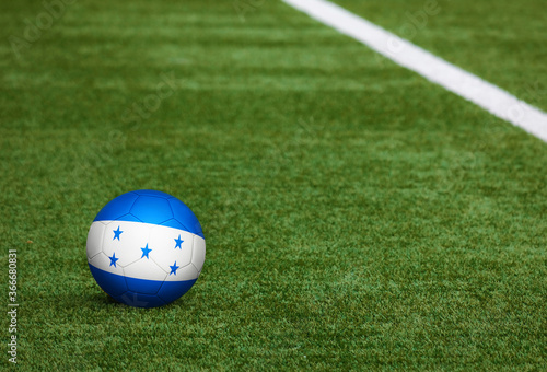 Honduras flag on ball at soccer field background. National football theme on green grass. Sports competition concept.