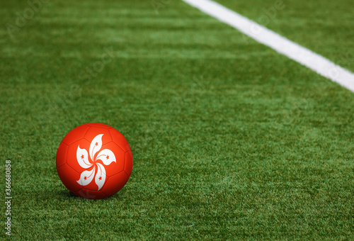Hong Kong flag on ball at soccer field background. National football theme on green grass. Sports competition concept.