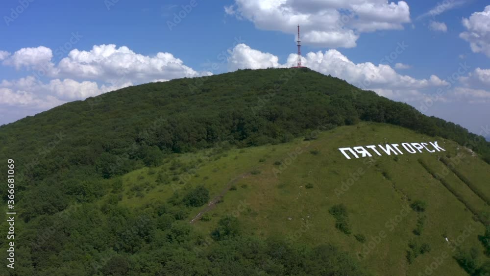 Aerial view of large white letters PYATIGORSK on the green Mashuk mountain. Summer sunny day. Blue sky and white clouds. Aerial view of large white letters PYATIGORSK on the green Mashuk mountain. Summer sunny day. Blue sky and white clouds.
