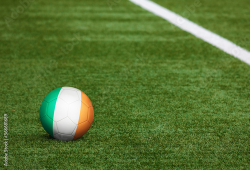 Ireland flag on ball at soccer field background. National football theme on green grass. Sports competition concept.