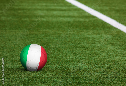 Italy flag on ball at soccer field background. National football theme on green grass. Sports competition concept.
