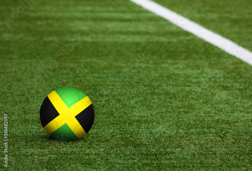 Jamaica flag on ball at soccer field background. National football theme on green grass. Sports competition concept.