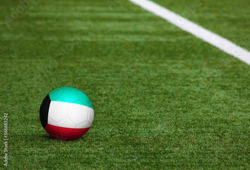 Kuwait flag on ball at soccer field background. National football theme on green grass. Sports competition concept.
