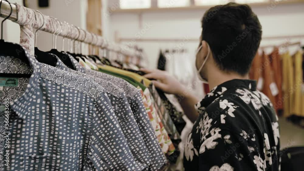 Hombre caucásico con camisa vintage comprando ropa en una tienda de ropa vintage con mascarilla covid coronavirus