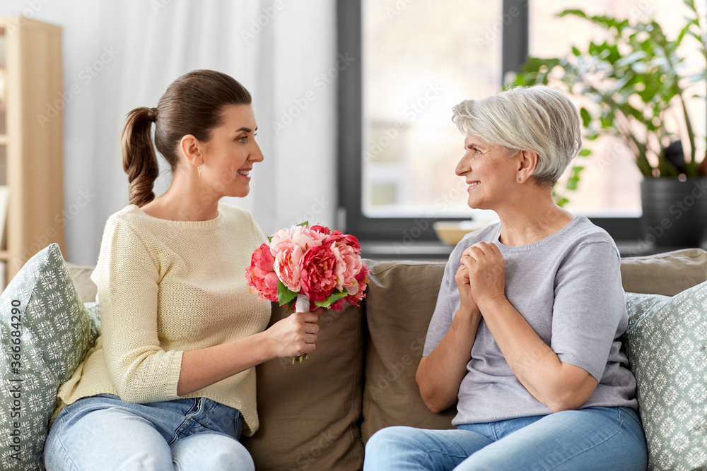 family, mother's day and birthday concept - happy smiling adult daughter giving flowers to her senior mother at home family, mother's day and birthday concept - happy smiling adult daughter giving flowers to her senior mother at home
