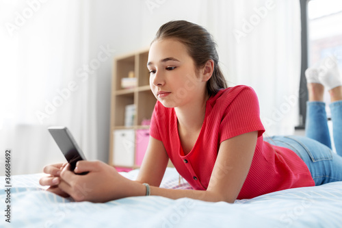 children, technology and communication concept - sad teenage girl texting on smartphone at home