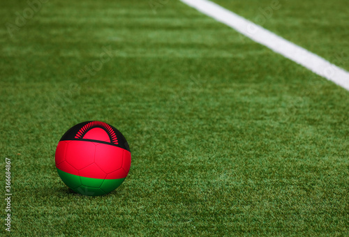 Malawi flag on ball at soccer field background. National football theme on green grass. Sports competition concept.