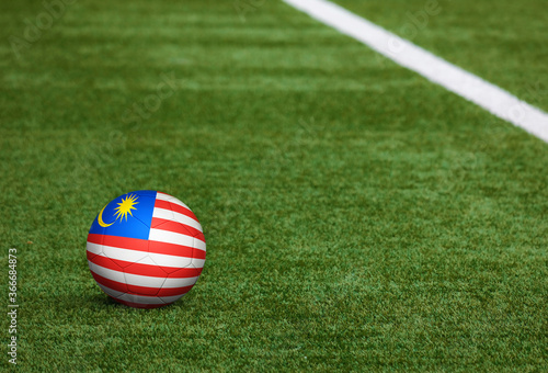 Malaysia flag on ball at soccer field background. National football theme on green grass. Sports competition concept.