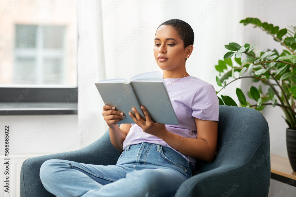 people and leisure concept - african american woman in glasses sitting on sofa and reading book at home people and leisure concept - african american woman in glasses sitting on sofa and reading book at home