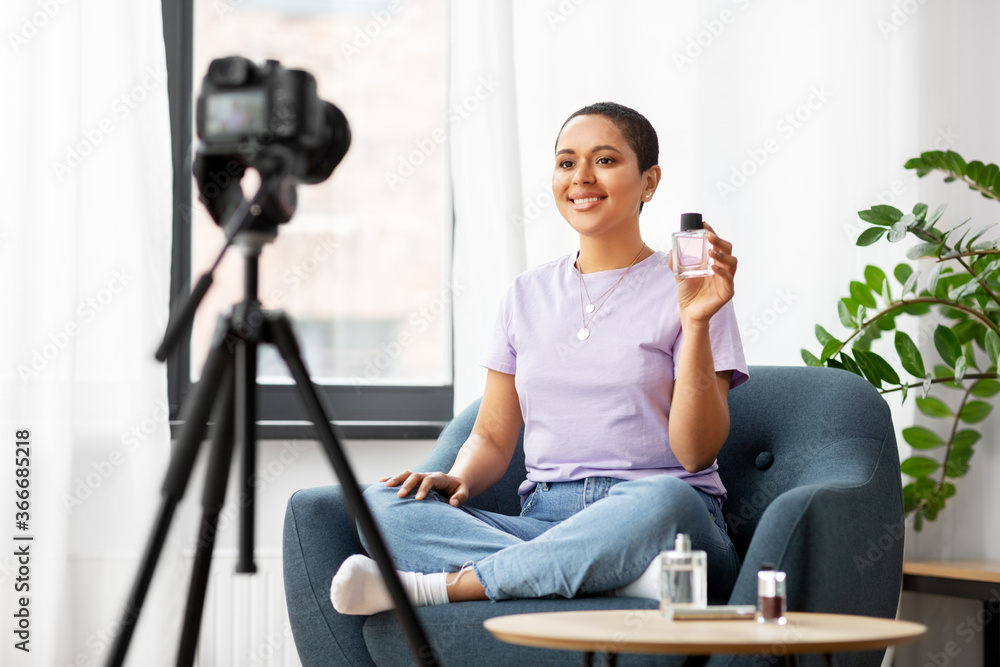 blogging, videoblog and people concept - happy smiling african american female beauty blogger with camera and perfume videoblogging at home blogging, videoblog and people concept - happy smiling african american female beauty blogger with camera and perfume videoblogging at home