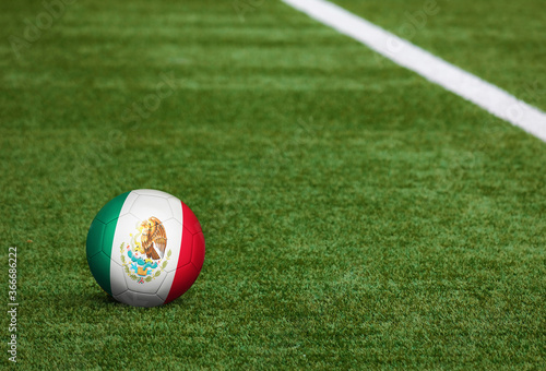 Mexico flag on ball at soccer field background. National football theme on green grass. Sports competition concept.