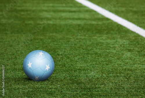Micronesia flag on ball at soccer field background. National football theme on green grass. Sports competition concept.
