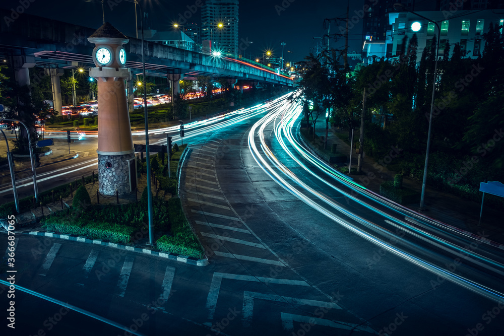 Car lights at night on the road going to the city with clock tower time. Aerial view of the speed traffic trails on motorway highway in Yannawa, Rama 3, Bangkok, Thailand. Long exposure abstract