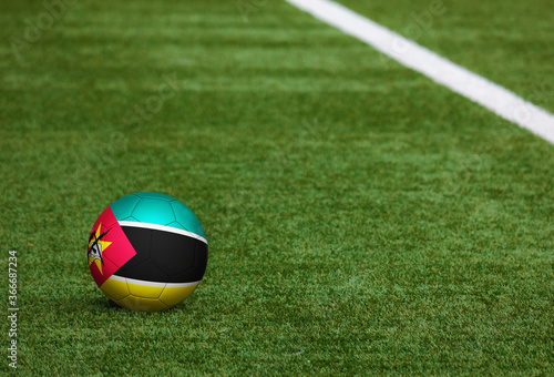 Mozambique flag on ball at soccer field background. National football theme on green grass. Sports competition concept.
