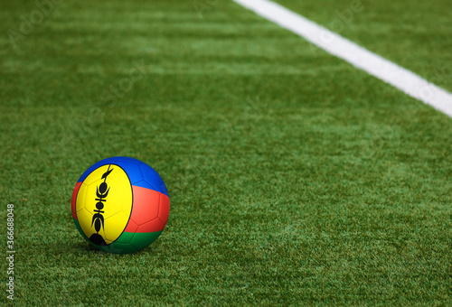 New Caledonia flag on ball at soccer field background. National football theme on green grass. Sports competition concept.