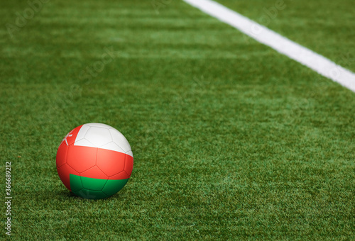 Oman flag on ball at soccer field background. National football theme on green grass. Sports competition concept.