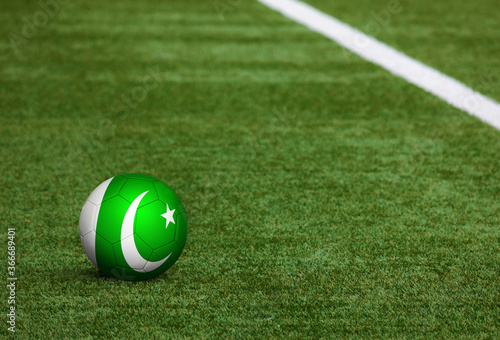 Pakistan flag on ball at soccer field background. National football theme on green grass. Sports competition concept.