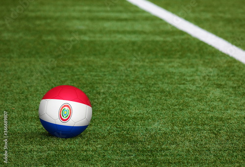Paraguay flag on ball at soccer field background. National football theme on green grass. Sports competition concept.