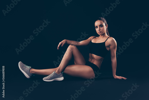 Portrait of her she nice-looking attractive sportive adorable content strong serious lady sitting on floor warming limbering up isolated over black background