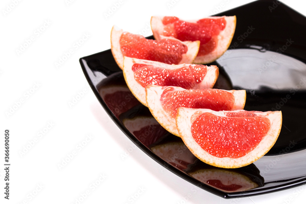 slices of grapefruit on a black plate on white background slices of grapefruit on a black plate on white background