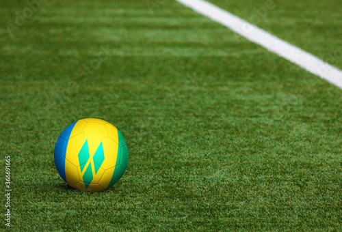 Saint Vincent And The Grenadines flag on ball at soccer field background. National football theme on green grass. Sports competition concept. © sezerozger