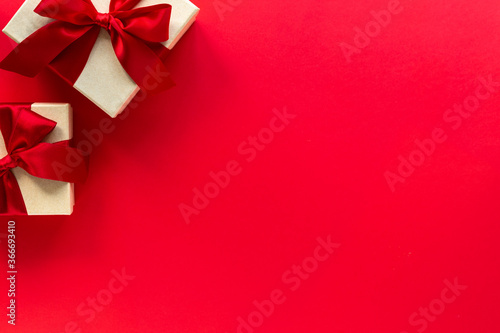 Two gift boxes with a red bow on a red background, top view with copy space