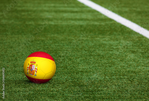 Spain flag on ball at soccer field background. National football theme on green grass. Sports competition concept.