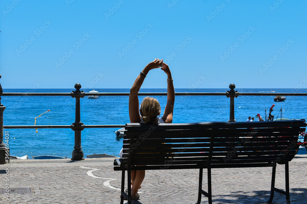 Woman sitting on a bench in front of the sea during the holidays