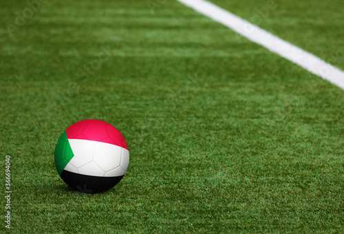 Sudan flag on ball at soccer field background. National football theme on green grass. Sports competition concept.