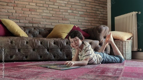 4k video footage of an adorable little boy looking at a playing cards album on the carpet, at home. Slow camera movement.