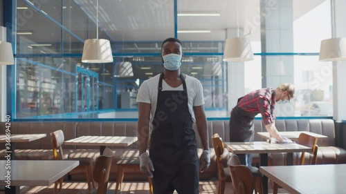 Portrait of african waiter in apron safety mask and glves walking in cafe photo