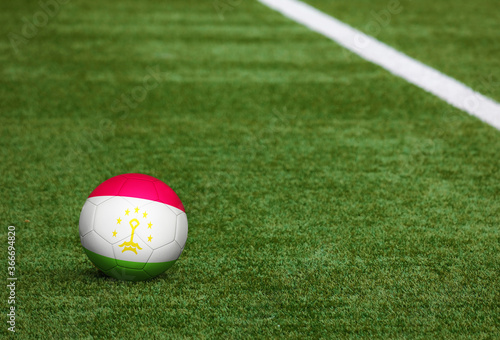 Tajikistan flag on ball at soccer field background. National football theme on green grass. Sports competition concept.