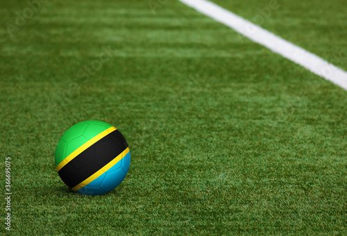 Tanzania flag on ball at soccer field background. National football theme on green grass. Sports competition concept.