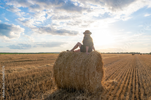 Girl at sunset in a field with hay.