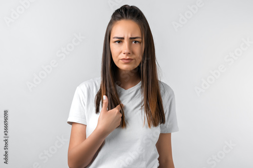 Me?! Portrait of indignant girl with long chestnut hair startled by offensive words, points at herself with for finger, opens mouth in surprisement, has dissatisfied expression, wears casual clothes © AstiMak