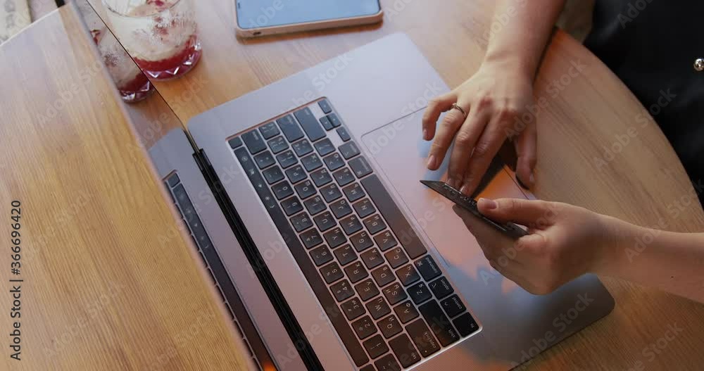 Young woman sitting on the coffeeshop, using laptop computer for online shopping with black platinum credit card on cafe background.