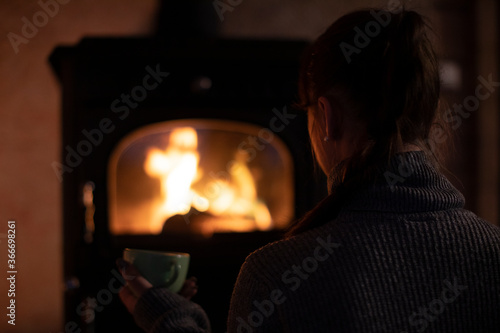 Introvert girl sits at home by the fireplace in the evening and drinks sweet cocoa. Reading books in the evenings at home. Warm and cozy atmosphere in the house.