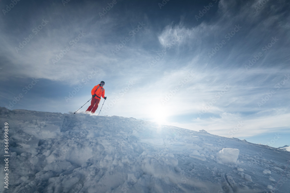 Athlete male skier jumps from a snow-covered slope against the backdrop of a mountain landscape of snow-covered mountains on a sunny day. The concept of winter sports wide angle
