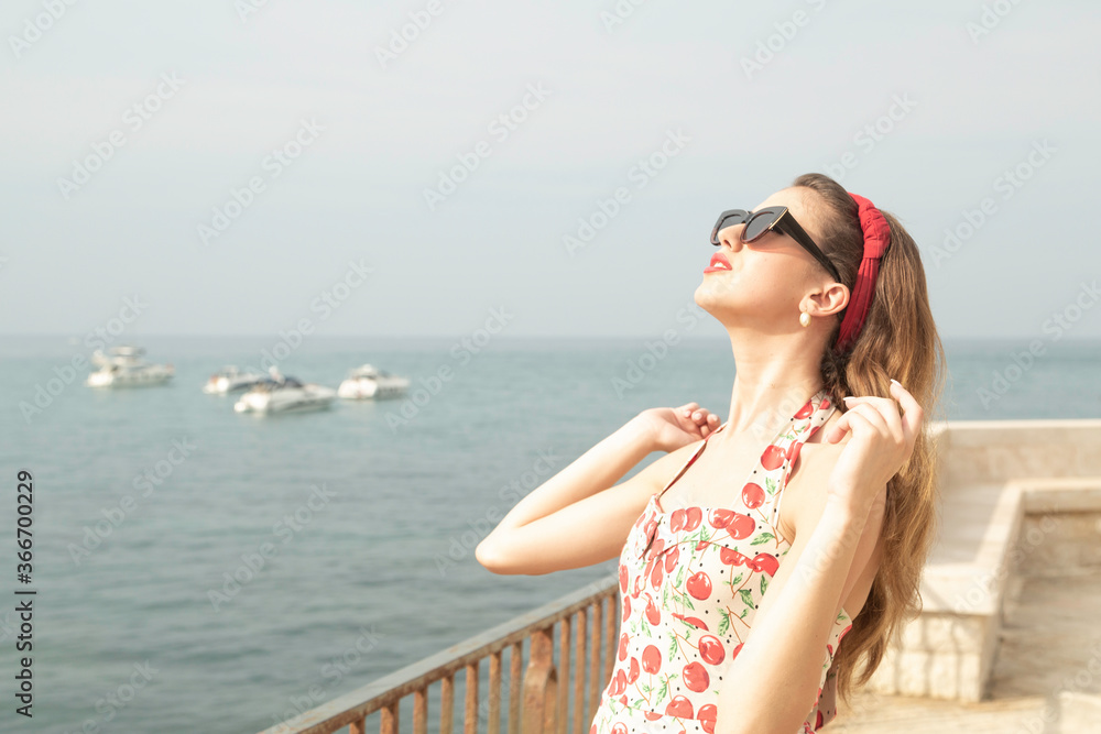 Trani, Barletta Andria Trani / Italy - June 26 2016: A beautiful italian woman with long light brown hair and red lipstick with vintage summer dot dress enjoying the rays of the sun